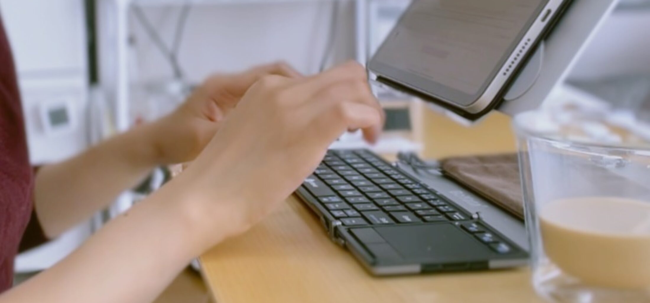 飲み物をそばに置き、タブレットのキーボードで作業する手元